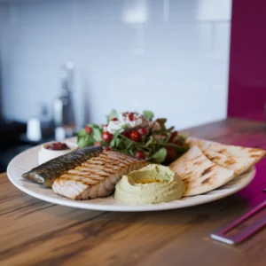 A-health-focused-Mediterranean-lunch-plate-featuring-grilled-fish-a-Greek-salad-a-small-portion-of-hummus-and-pita-bread