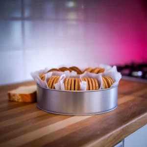 A-neatly-arranged-metal-tin-with-layers-of-cookies-separated-by-parchment-paper-with-a-small-slice-of-bread-placed-to-one-side