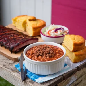 A-photo-of-baked-beans-with-ground-beef-served-with-grilled-ribs-coleslaw-and-cornbread-presented-on-a-rustic-table-for-a-homestyle-feel