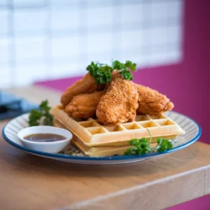 A-plate-of-golden-waffles-topped-with-crispy-chicken-tenders-garnished-with-fresh-parsley-and-a-small-dish-of-maple-syrup-on-the-side