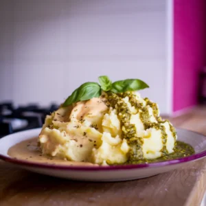 A-serving-of-mashed-potatoes-with-half-covered-in-creamy-garlic-sauce-and-the-other-half-drizzled-with-vibrant-green-pesto-garnished-with-fresh-basil-leaves