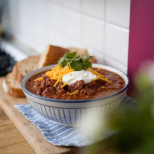 A-bowl-of-steak-chili-topped-with-sour-cream-shredded-cheese-and-fresh-cilantro-paired-with-a-side-of-crusty-bread