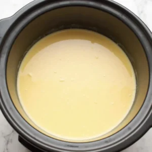 A creamy sauce being thickened with parmesan and cornstarch slurry in a crockpot.