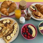 Sweet breakfast table with crepes, croissants, and smoothie bowls.